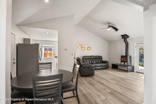 dining space with light wood-type flooring, a wood stove, ceiling fan, and lofted ceiling