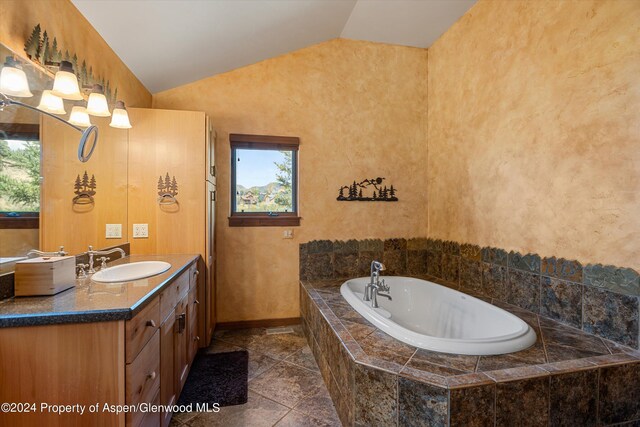 bathroom featuring vanity, tiled bath, and lofted ceiling