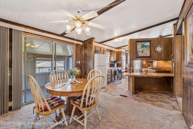 dining area featuring ceiling fan, light carpet, lofted ceiling, and wooden walls