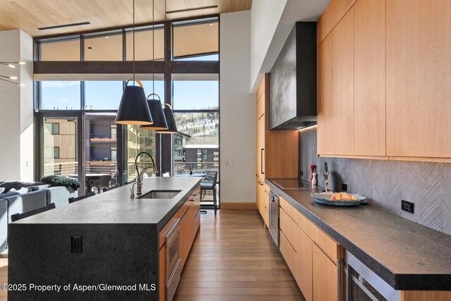 kitchen featuring tasteful backsplash, sink, wall chimney range hood, floor to ceiling windows, and a center island with sink