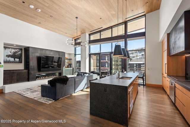 kitchen featuring sink, wood ceiling, a wall of windows, a center island with sink, and decorative light fixtures