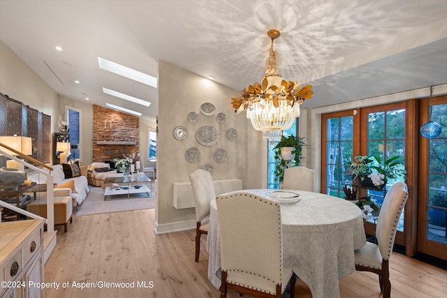 dining space with french doors, lofted ceiling with skylight, a notable chandelier, light hardwood / wood-style floors, and a stone fireplace