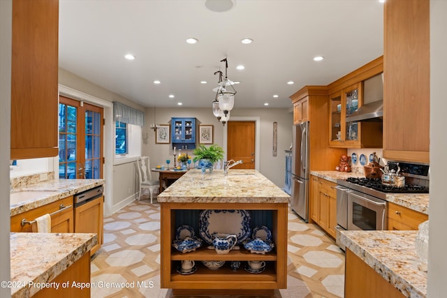 kitchen featuring sink, wall chimney exhaust hood, an island with sink, appliances with stainless steel finishes, and light stone counters