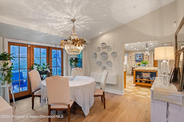 dining room featuring a notable chandelier, vaulted ceiling, light wood-type flooring, and french doors