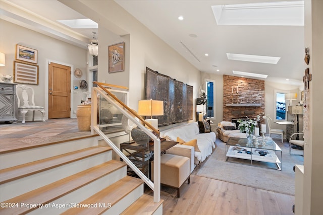 living room with a stone fireplace, lofted ceiling with skylight, and hardwood / wood-style flooring