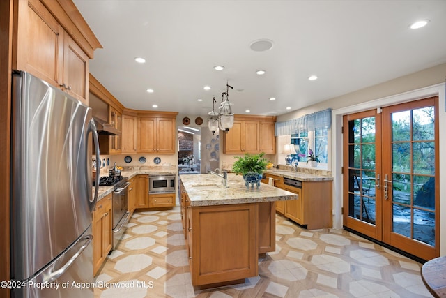 kitchen with french doors, stainless steel appliances, sink, pendant lighting, and an island with sink