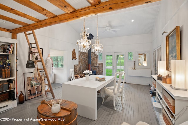 dining room featuring a wood stove, light hardwood / wood-style flooring, lofted ceiling with beams, and ceiling fan with notable chandelier