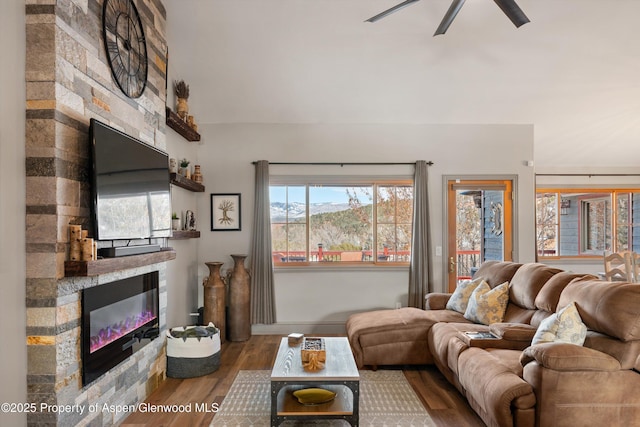 living room featuring ceiling fan, hardwood / wood-style floors, and a stone fireplace