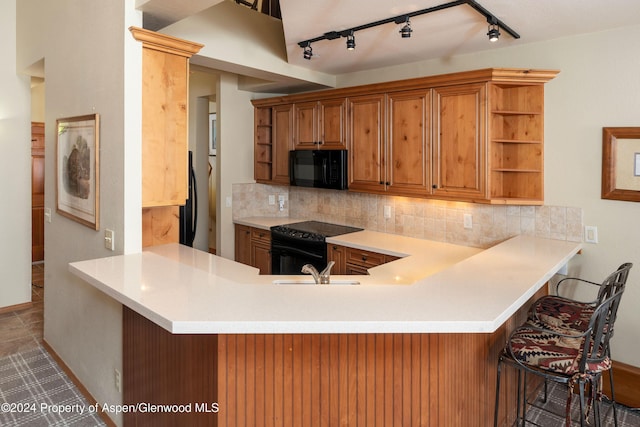 kitchen with sink, a kitchen breakfast bar, kitchen peninsula, decorative backsplash, and black appliances