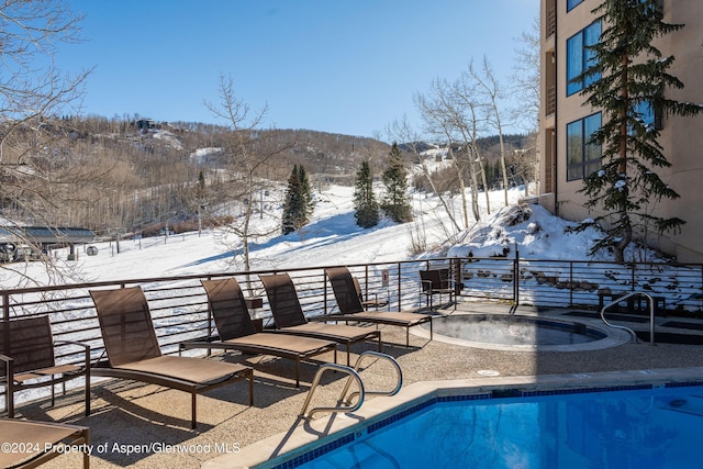 snow covered pool featuring a mountain view and a community hot tub