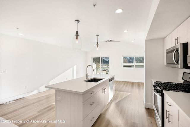 kitchen with sink, appliances with stainless steel finishes, a kitchen island with sink, hanging light fixtures, and vaulted ceiling