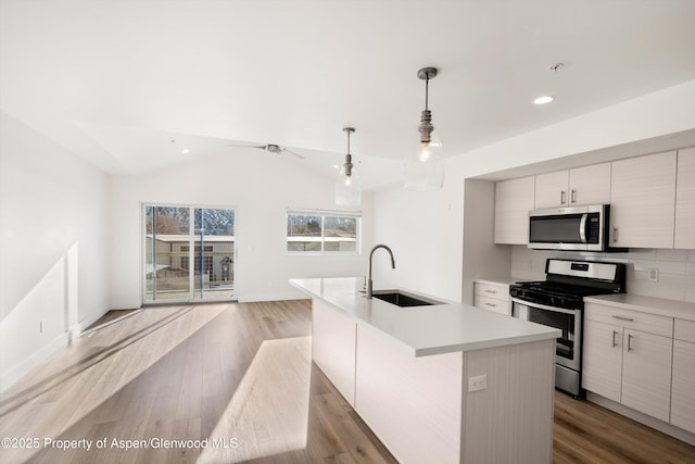 kitchen featuring sink, appliances with stainless steel finishes, an island with sink, decorative light fixtures, and vaulted ceiling