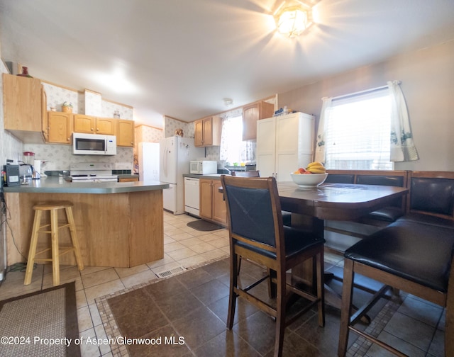 kitchen featuring light brown cabinets, white appliances, tile patterned floors, tasteful backsplash, and kitchen peninsula