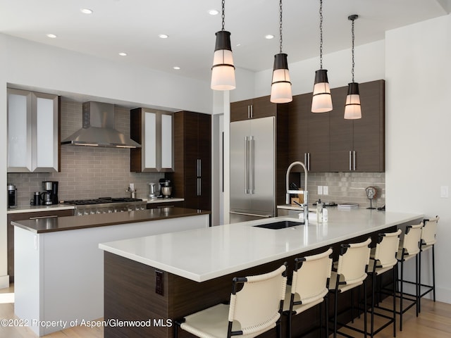 kitchen with a breakfast bar area, appliances with stainless steel finishes, wall chimney exhaust hood, decorative light fixtures, and tasteful backsplash