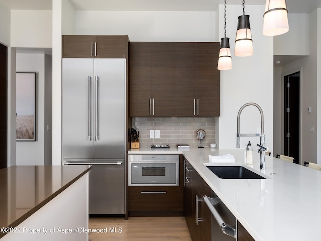 kitchen featuring hanging light fixtures, stainless steel appliances, tasteful backsplash, dark brown cabinets, and sink