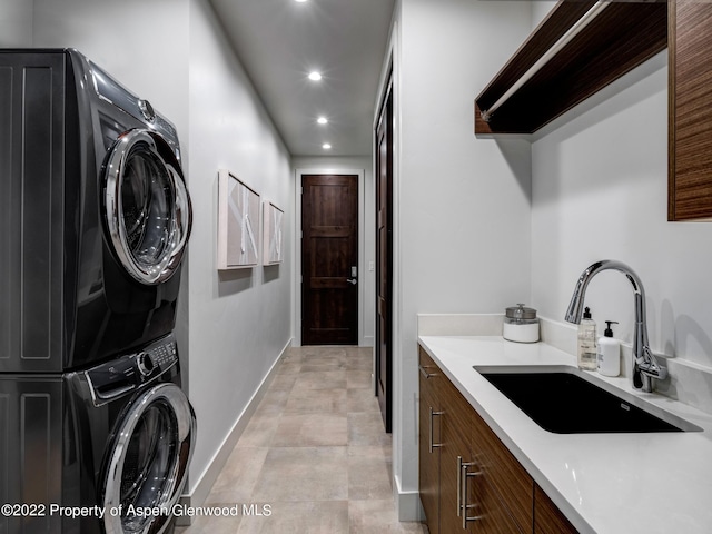 laundry area with stacked washer and dryer, cabinets, and sink