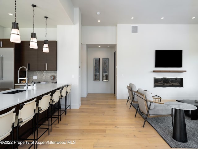 kitchen with decorative light fixtures, decorative backsplash, high end fridge, dark brown cabinets, and sink