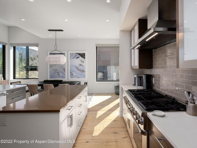 kitchen with decorative light fixtures, white cabinetry, wall chimney exhaust hood, a kitchen island, and double oven range