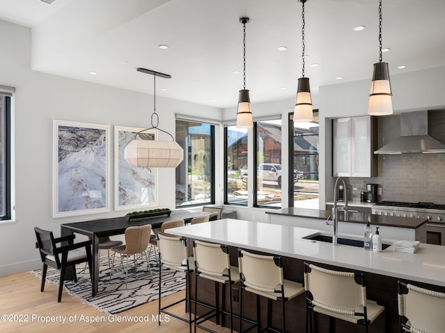 kitchen featuring sink, decorative light fixtures, light hardwood / wood-style flooring, backsplash, and wall chimney range hood