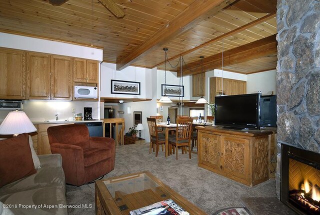 living room with beamed ceiling, a stone fireplace, wooden ceiling, and light carpet