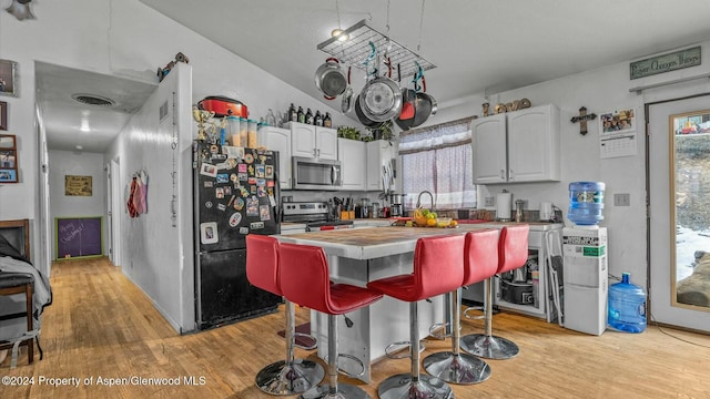 kitchen with white cabinetry, a breakfast bar, light wood-type flooring, and appliances with stainless steel finishes