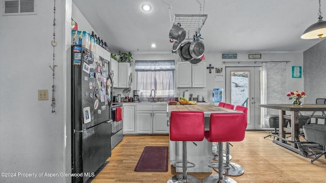 kitchen featuring black refrigerator, light wood-type flooring, a healthy amount of sunlight, white cabinets, and a breakfast bar area