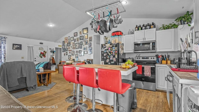 kitchen with a kitchen breakfast bar, light hardwood / wood-style flooring, lofted ceiling, white cabinets, and appliances with stainless steel finishes