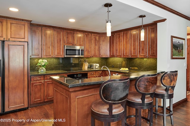 kitchen with paneled refrigerator, a breakfast bar area, hanging light fixtures, and dark wood-type flooring