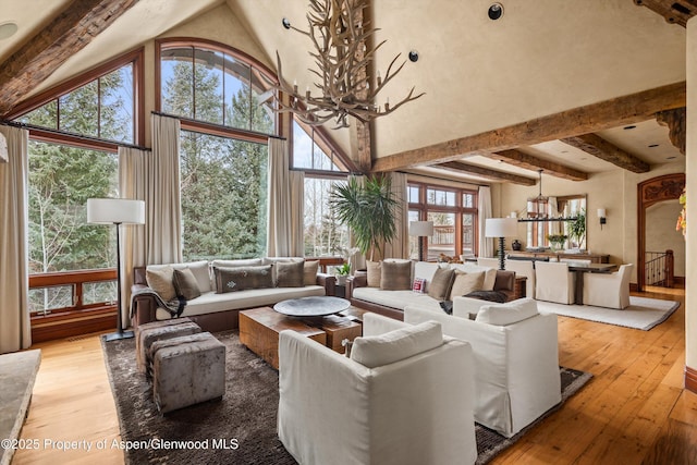 living area with an inviting chandelier, beam ceiling, a high ceiling, and hardwood / wood-style floors