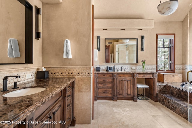 full bathroom featuring a bathing tub, tile walls, two vanities, and a sink