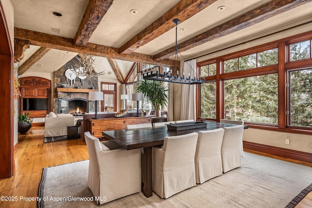 dining room with baseboards, vaulted ceiling with beams, light wood-type flooring, a fireplace, and a chandelier