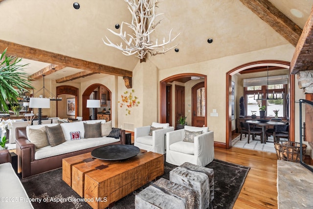 living room featuring arched walkways, a chandelier, beam ceiling, and light wood-style floors