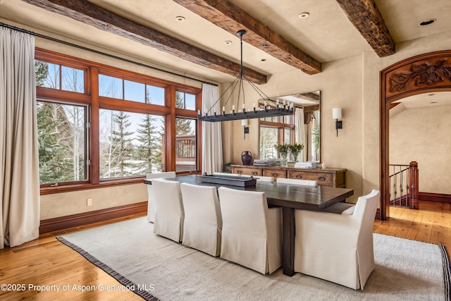 dining room with light wood finished floors, baseboards, beam ceiling, and an inviting chandelier