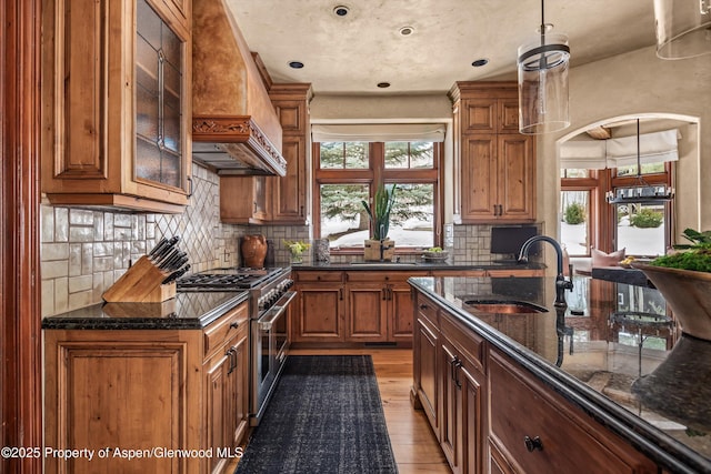 kitchen with premium range hood, a sink, brown cabinetry, stainless steel range, and plenty of natural light