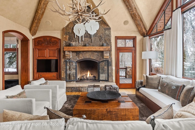 living area featuring a stone fireplace, beamed ceiling, plenty of natural light, and wood finished floors