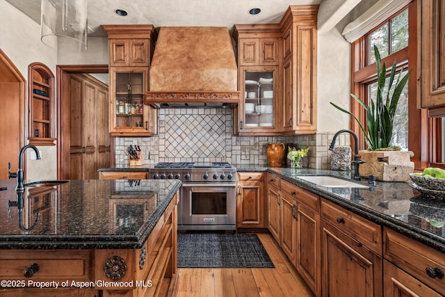 kitchen featuring a sink, premium range hood, high end stove, and brown cabinets