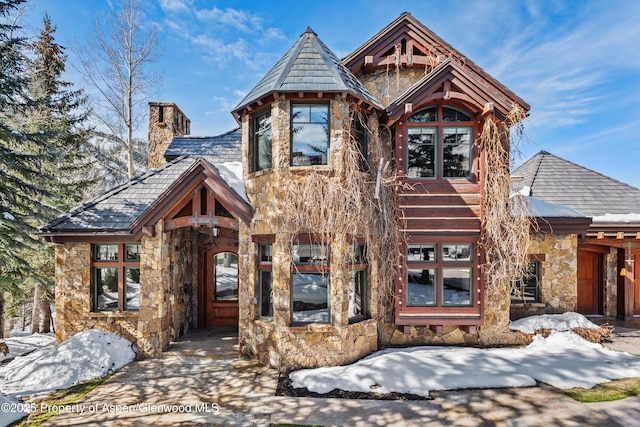 view of front of house with a high end roof, stone siding, and a chimney