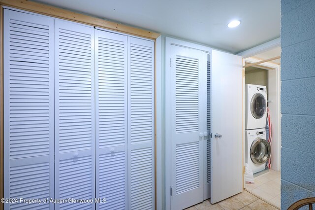 laundry area with light tile patterned flooring and stacked washer / dryer