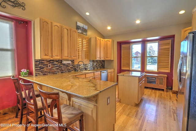 kitchen featuring a center island, a kitchen breakfast bar, kitchen peninsula, vaulted ceiling, and appliances with stainless steel finishes