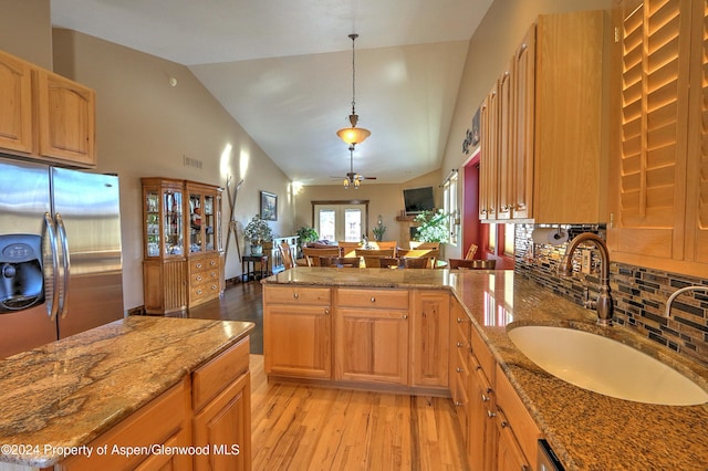 kitchen with ceiling fan, sink, light stone counters, stainless steel fridge, and decorative light fixtures