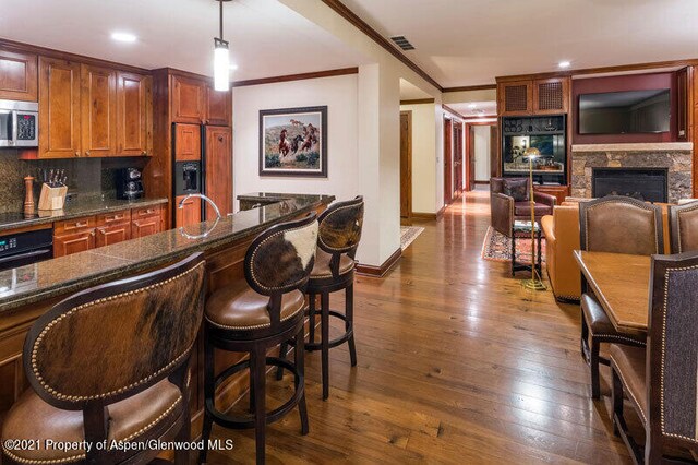 bar with dark wood-style floors, crown molding, black appliances, a fireplace, and backsplash