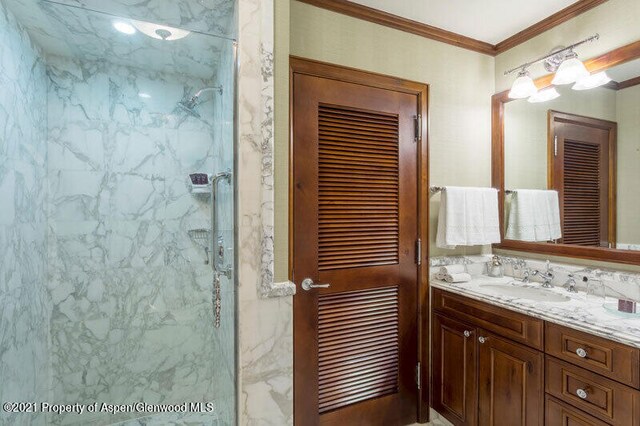 bathroom featuring ornamental molding, a marble finish shower, and vanity