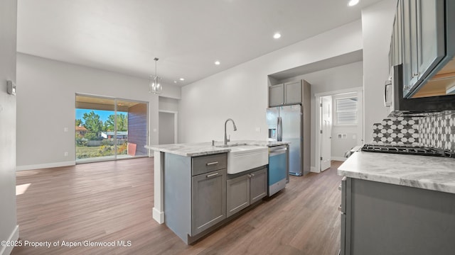 kitchen featuring light stone counters, decorative light fixtures, stainless steel appliances, gray cabinets, and a center island with sink