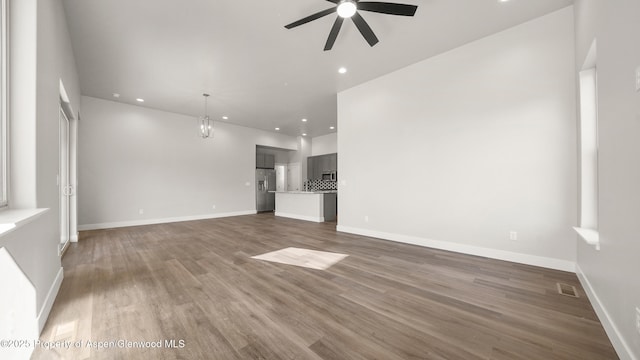 unfurnished living room featuring recessed lighting, ceiling fan with notable chandelier, dark wood-style flooring, visible vents, and baseboards