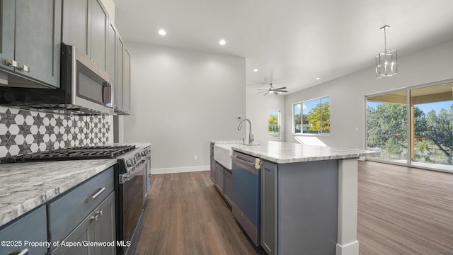 kitchen with stainless steel appliances, gray cabinets, a center island with sink, and hanging light fixtures