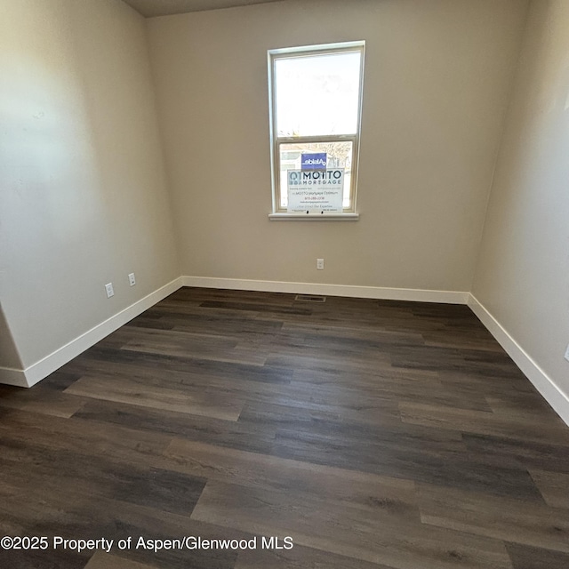 unfurnished room with dark wood-style floors, visible vents, and baseboards