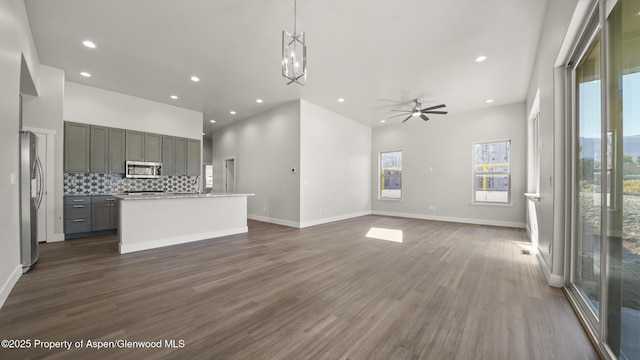 unfurnished living room with dark wood-style floors, ceiling fan with notable chandelier, baseboards, and recessed lighting