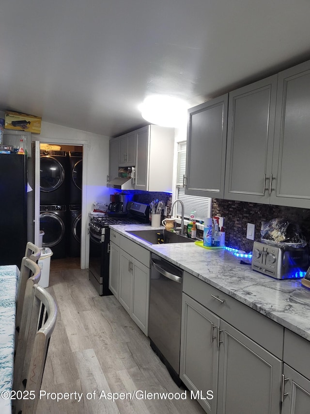 kitchen featuring sink, light hardwood / wood-style flooring, gray cabinetry, stainless steel appliances, and stacked washer / dryer