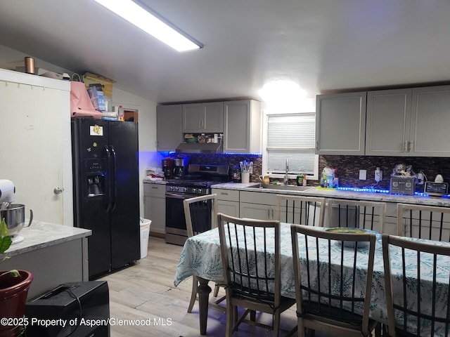 kitchen featuring gray cabinets, lofted ceiling, sink, stainless steel gas range oven, and black refrigerator with ice dispenser