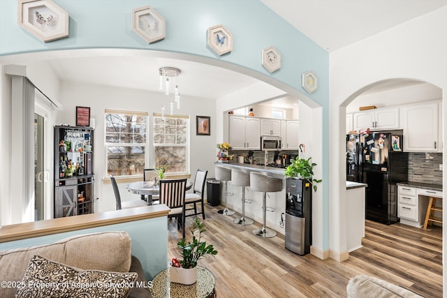 interior space featuring pendant lighting, white cabinetry, decorative backsplash, light hardwood / wood-style floors, and black refrigerator with ice dispenser